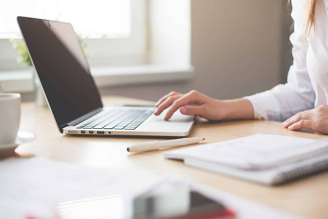 Imagine a highly productive workspace—a person using a laptop to craft Google Posts, surrounded by essential tools: a notebook, pen, and cup on the wooden desk. Sunlight streaming through the window enhances focus and productivity, serving as your secret weapon for success.